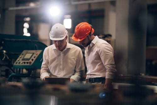 Two engineers wearing hard hats review equipment inside an industrial facility.